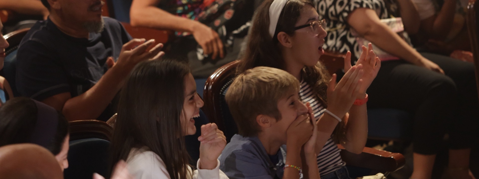 Excited kids and families clapping and cheering during a live magic show