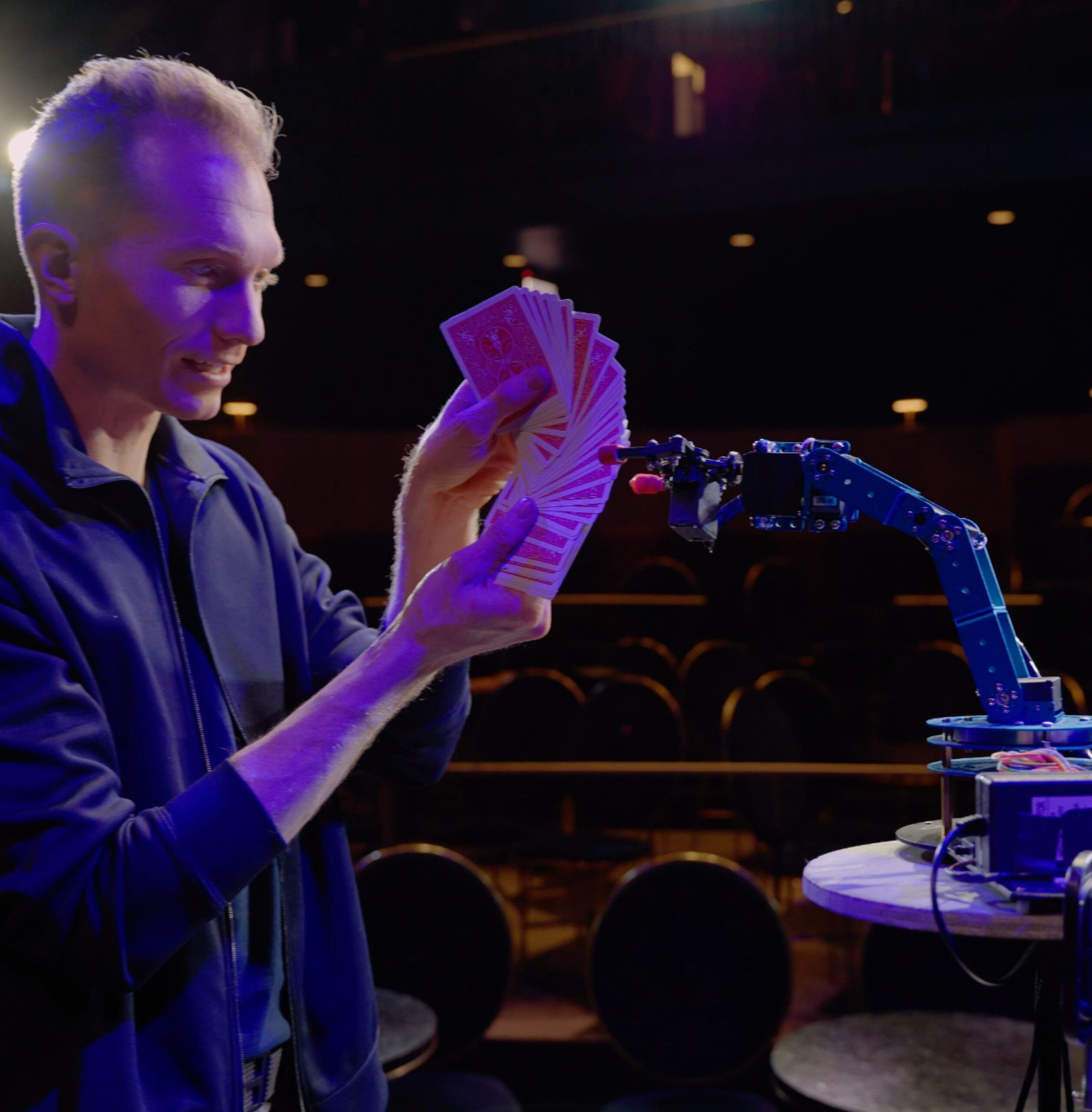 Trigg performing a card trick with a robot arm. 